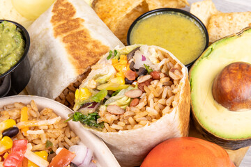A cut open Mexican burrito with an avocado and dipping sauce
