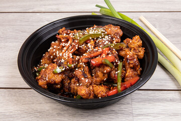 Chinese sesame chicken in a black plastic takeout dish with chopsticks