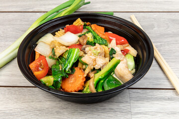Chinese mixed vegetables with chicken in a black plastic takeout dish with chopsticks