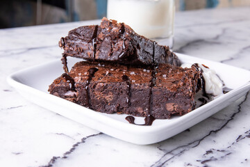 large chocolate brownies drizzled with chocolate on a plate on a white granite table