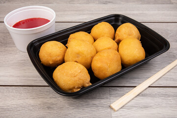 Chinese chicken balls with chicken in a black plastic takeout dish with red sauce and chopsticks