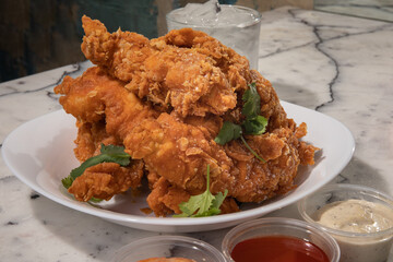 Southern fried chicken tenders with dipping sauces on a white restaurant plate