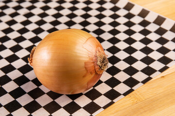 a white cooking onion on black checkered paper in a kitchen