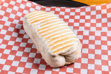 A rolled and toasted Mexican burrito on red checker paper
