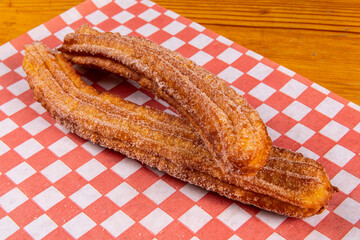 A single Mexican deep fried sweet churros on red checked paper
