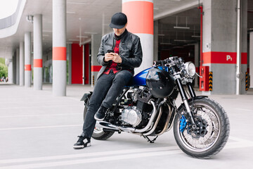 Man in leather jacket sits on custom motorcycle while texting