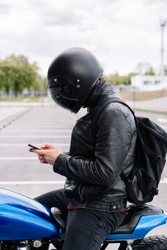 Rider in black helmet checks phone while sitting on blue motorcycle