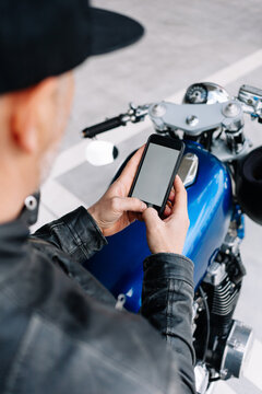 Person using phone while standing by a blue motorcycle outdoors