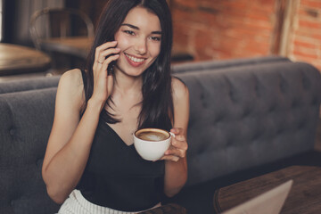 Business woman working on a laptop, using phone and drinking coffee in a cafe.