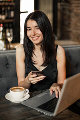 Business woman working on a laptop, using phone and drinking coffee in a cafe.