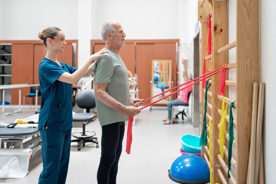 Senior man guided by physiotherapist using resistance bands