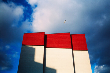 Red geometric building under stormy sky with bird