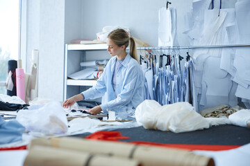 Professional clothing woman creator arranging pattern pieces meticulously during daylight in studio
