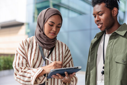 Two young professionals collaborate using a tablet outdoors.