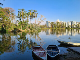 Canoes anchored on a lake with reflections of the surrounding trees and city buildings