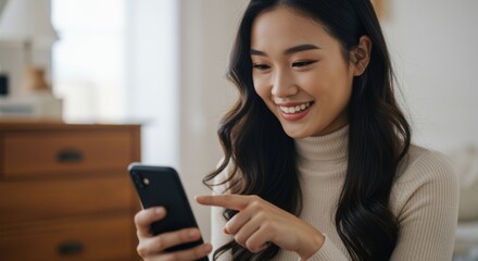 Young Asian woman smiling while looking at her smartphone screen indoors
