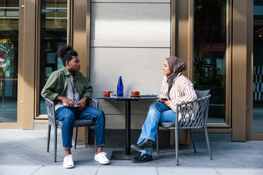 Young couple conversing over coffee at an outdoor cafe.