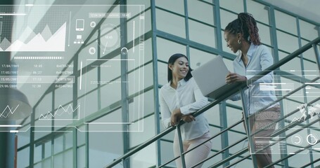 Holding laptop, two women discussing data overlay in atrium by metal rail, office wear, copy space