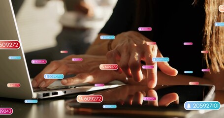 Typing hands in dark longsleeve pressing laptop keys at desk, tapping tablet with numeric badges
