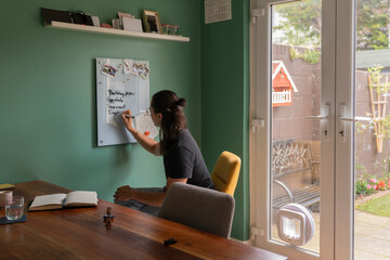 Man Writes Grocery List on Glass Board in Kitchen Against Green Wall