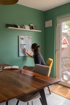 Man Writes Grocery List on Glass Board at Home Kitchen With Green Wall