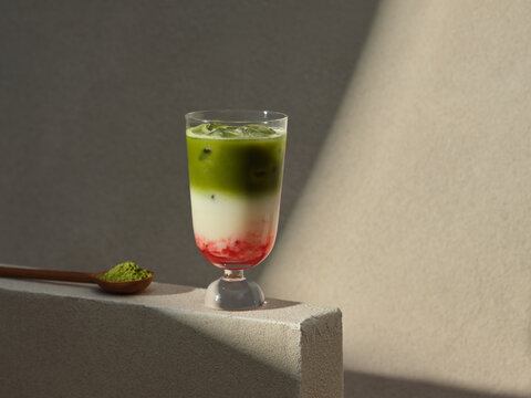 A layered matcha strawberry latte with ice, served with a wooden spoon