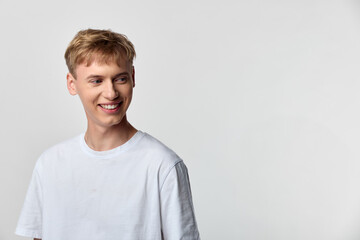 Smiling young man in a white casual t shirt stands in a clean studio backdrop, radiating friendly confidence and simple charm for lifestyle, fashion, and marketing campaigns.