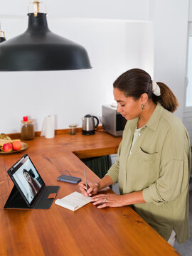 Woman writing notes during video call with colleague 