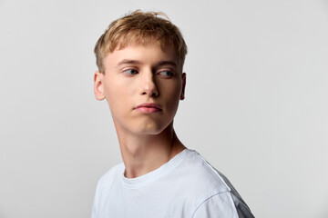 Man with short blond hair wearing a white shirt looks away against a neutral studio backdrop,...