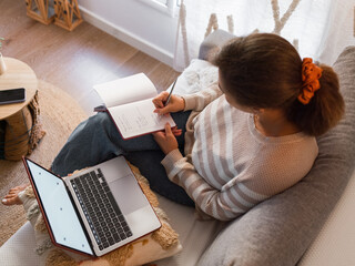 Woman taking notes near laptop at home