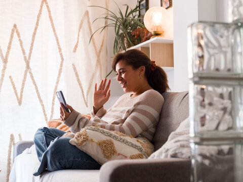 Woman Smiling and Waving While Using Smartphone at Home