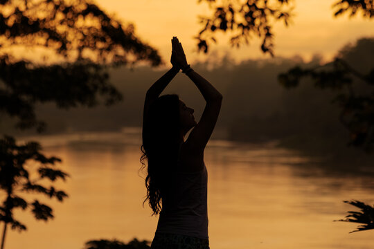 Silhouette of woman meditating in tropical rainforest at sunrise