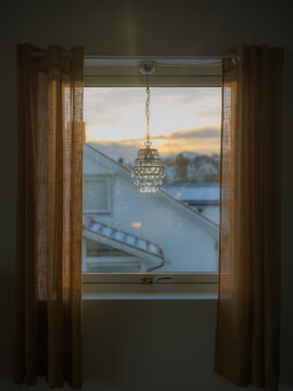Window with retro lamp and curtains overlooking snowy village 