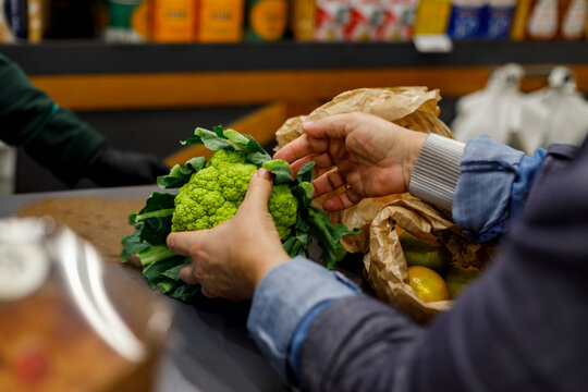 Person Places Produce on Conveyor at Grocery Store Checkout