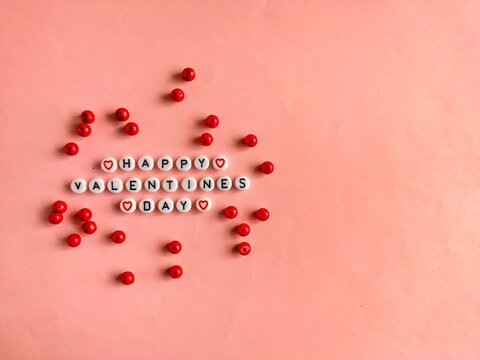happy valentine&rsquo;s day text made of letter beads with red bead decoration on pink background