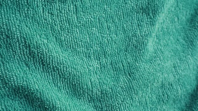 Close-up of a textured teal fabric with a soft, woven pattern and gentle folds against a white background.