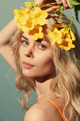 Beautiful young woman with long blonde hair and yellow flowers, showcasing vibrant spring vibes and natural beauty in a soft pastel background.
