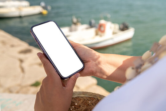 Hands Holding a Smartphone Near Boats in a Peaceful Harbor