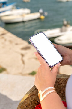 Woman Holding Smartphone by the Water With Boats in the Background