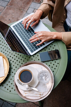 Woman working on laptop at a cafe table with coffee and phone