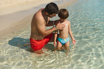 Dad Applying Sunscreen to Son in Shallow Sea