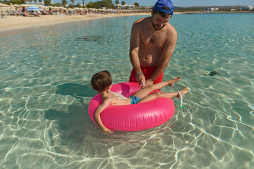 Father Applying Sunscreen to Son in Inflatable Ring at Beach