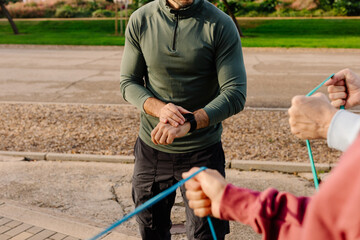 Anonymous senior coach observes an older couple exercising outdoors
