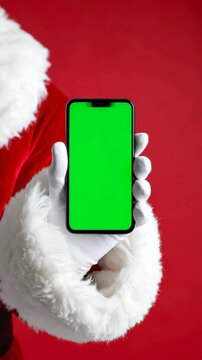 Festive character in red outfit holds a mobile phone with a green screen display against a red background indoors