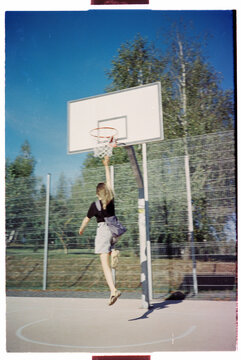 Girl performing a slam dunk at an outdoor basketball court