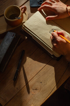 Hands Drawing in Notebook with Coffee Cup Nearby