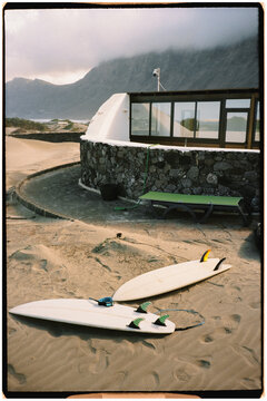 Couple of surfboards lying on the sand near a kiosk on a beach