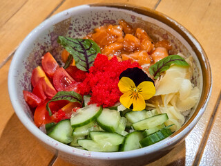 Top view of a colorful salmon poke bowl with fresh vegetables, flying fish roe and rice, garnished with edible pansies flower