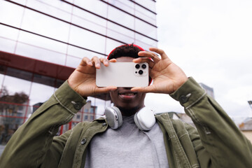 Young black man taking photo on smartphone outdoors on city street