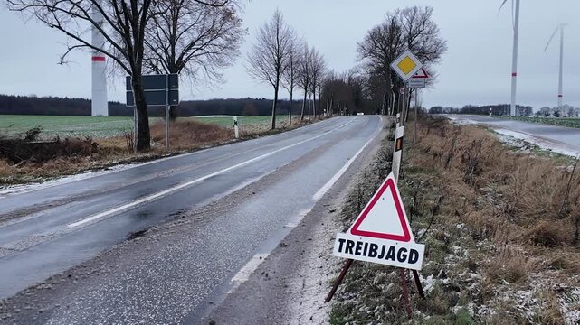 Rural roadside scene in winter featuring a German warning sign reading &ldquo;Treibjagd,&rdquo; indicating a driven hunt in progress.
